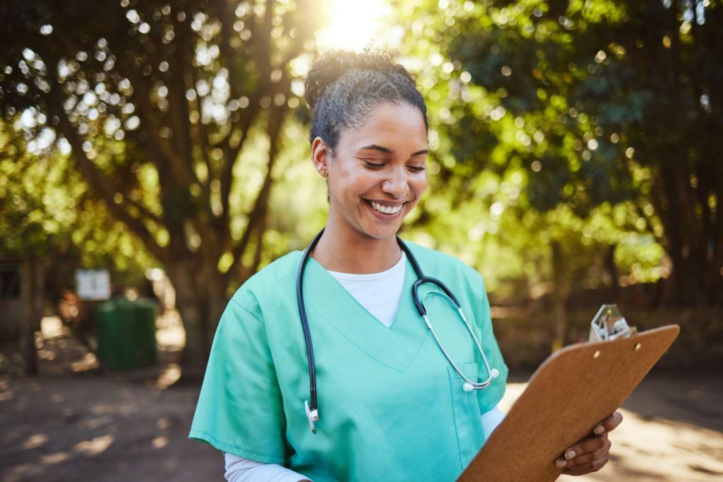 Nurse smiling and holding a clipboard while standing outside 