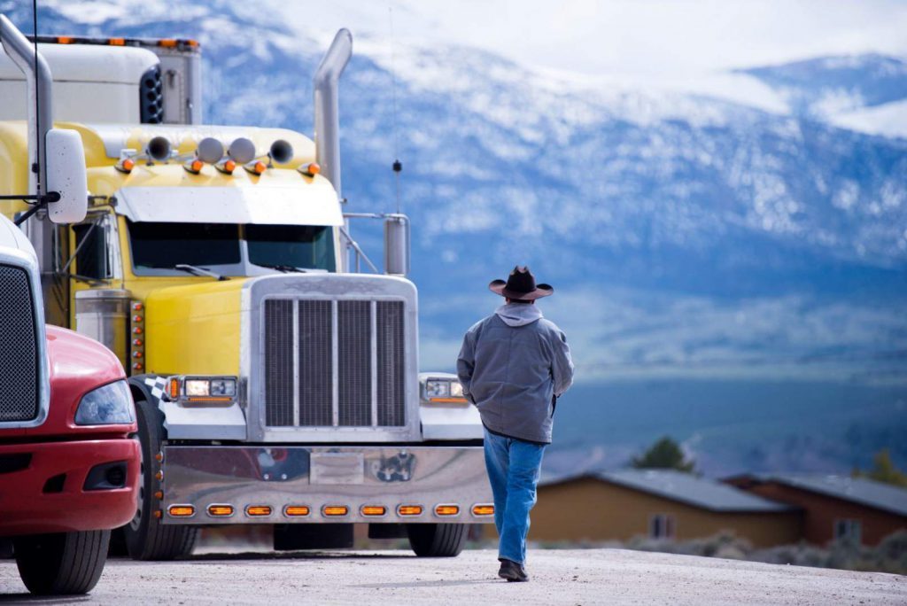 A truck driver walking back to his yellow truck near the mountains 