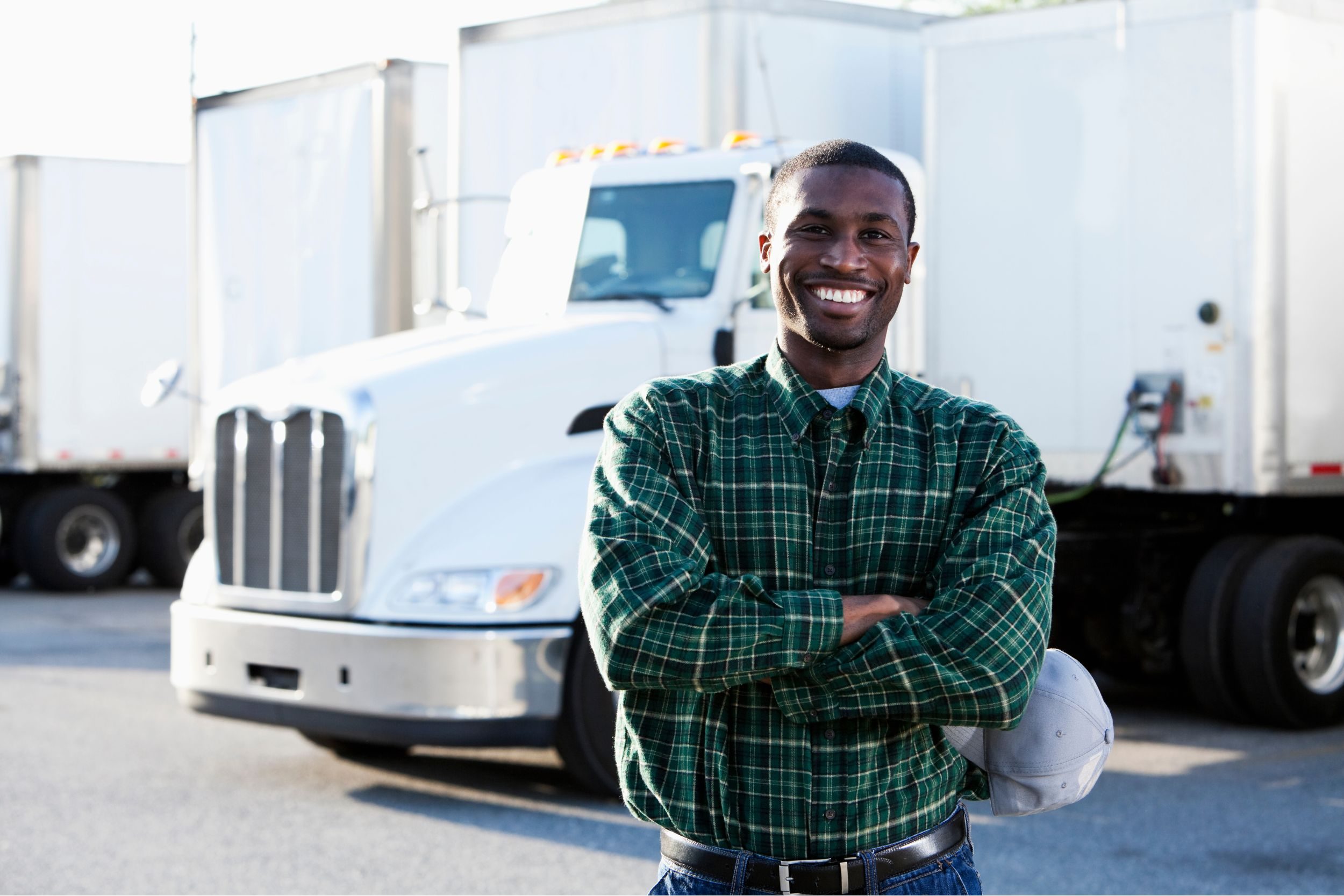 A man standing in front of a white semi truck with his arms crossed and smiling at the camera