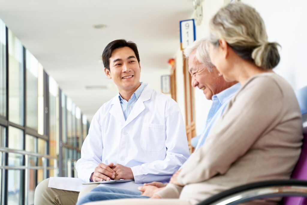A male physician sitting down and smiling at an elderly couple sitting beside him
