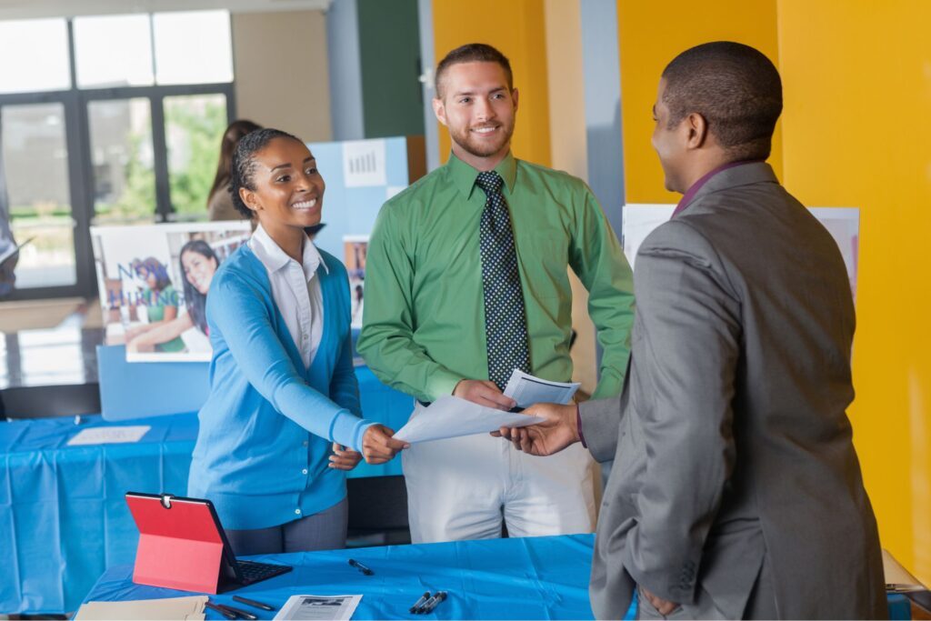 A man and woman handing a man papers at a job fair 