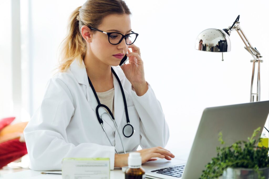 A female physician calling someone on the phone while scrolling on her computer