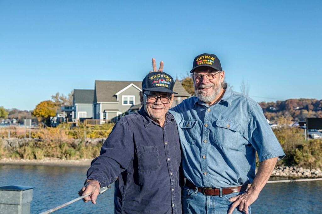Two older veterans wearing their military hats and smiling at the camera