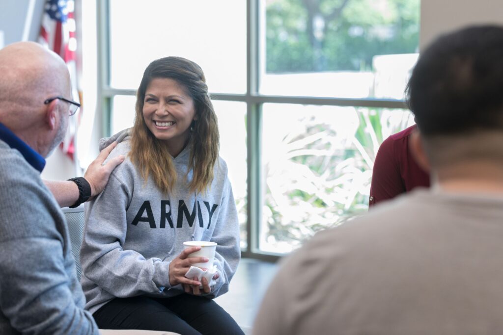 A woman in an army sweatshirt smiling at a man patting her shoulder