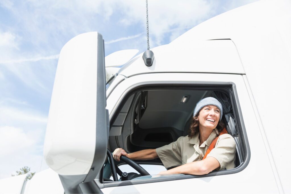 A female truck driver in the driver's seat of her truck smiling