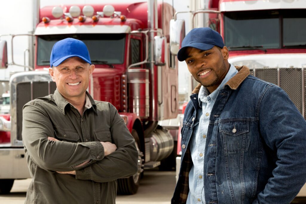 Two truck drivers smiling at the camera in front of their red semi-trucks
