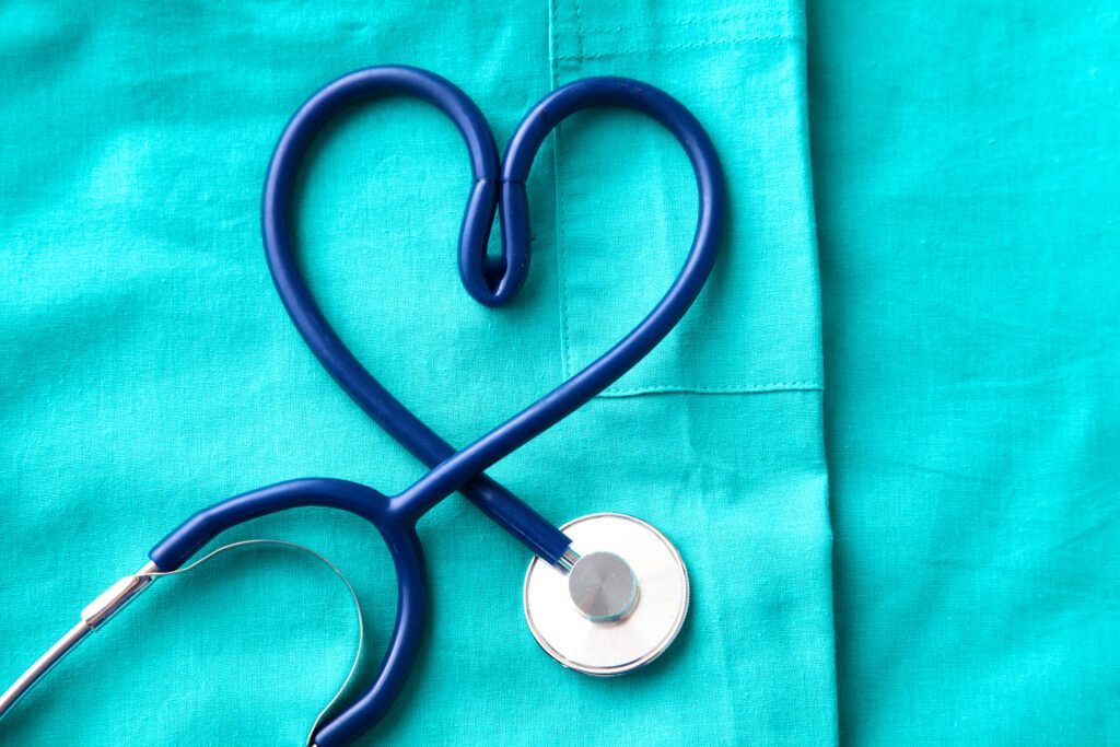 A stethoscope shaped into a heart laying on a pair of folded scrubs