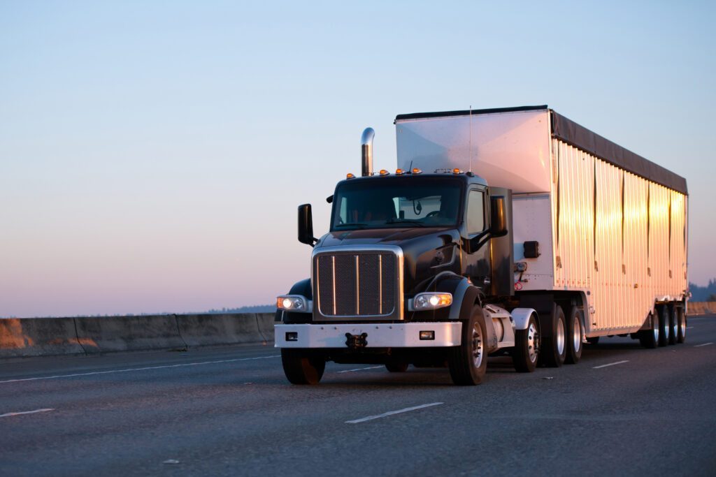 Dark big rig semi truck with bulk trailer running during sunset