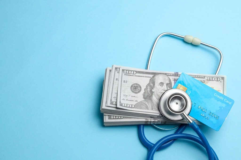 Stack of cash dollars and credit card with stethoscope on blue background. 