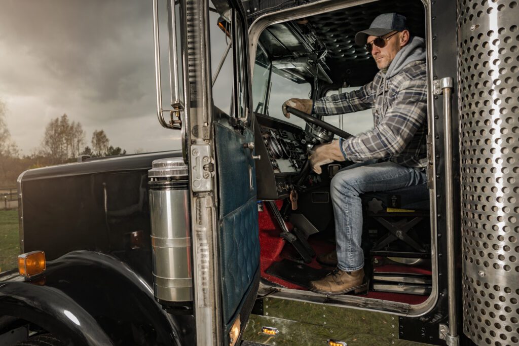 Male trucker sitting in the driver's seat of his truck with the door open