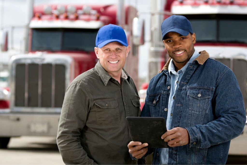 Two truck drivers standing in front of trucks and smiling at the camera