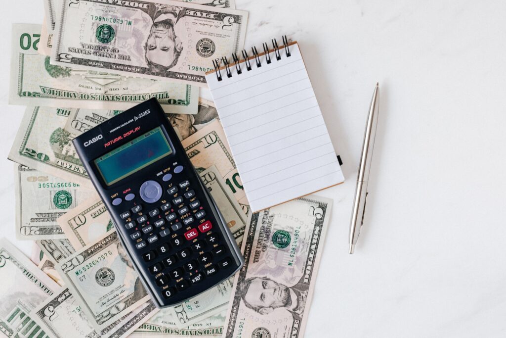 A calculator and notebook with pen sitting on top of cash
