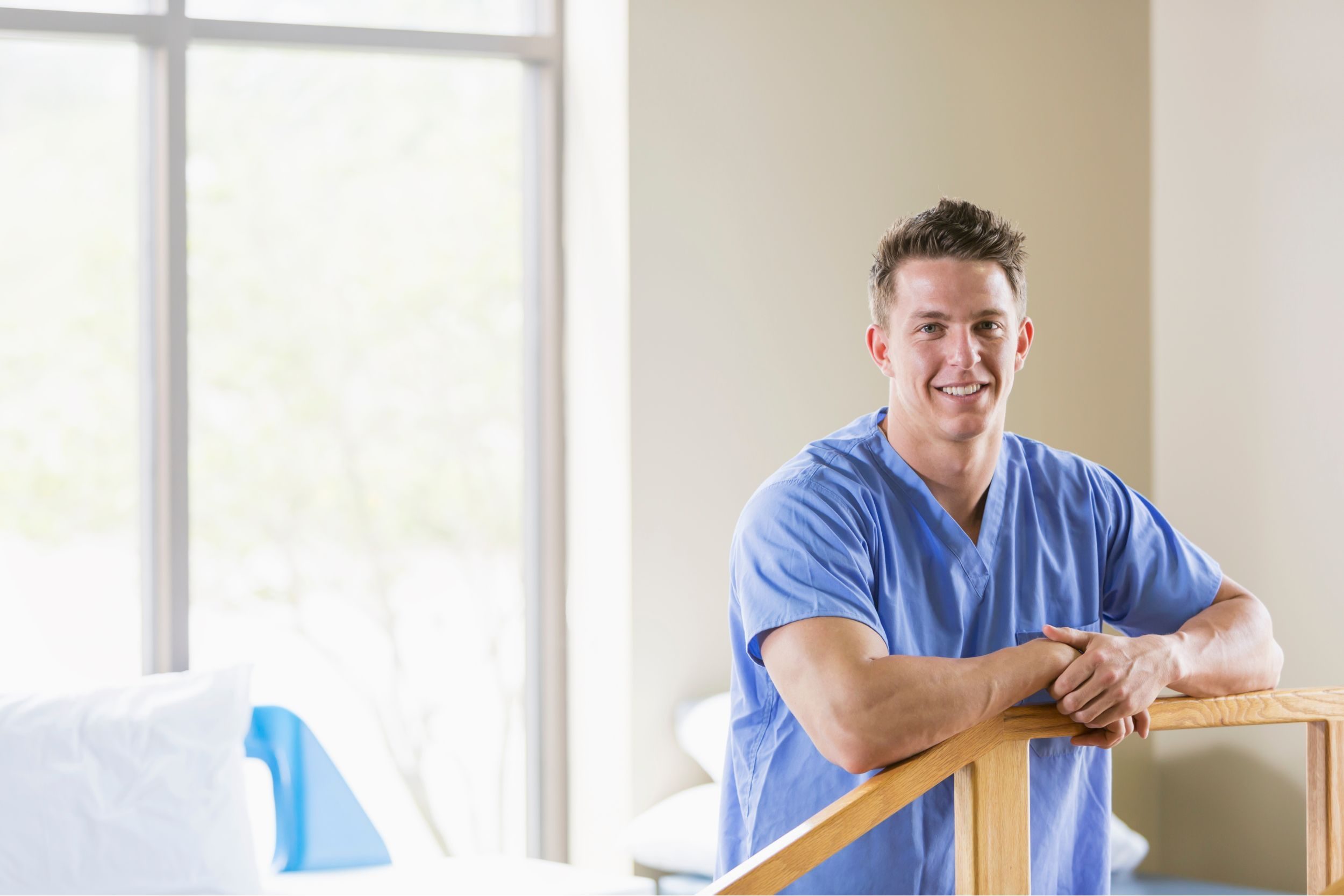 A male young healthcare worker in scrubs smiling at the camera