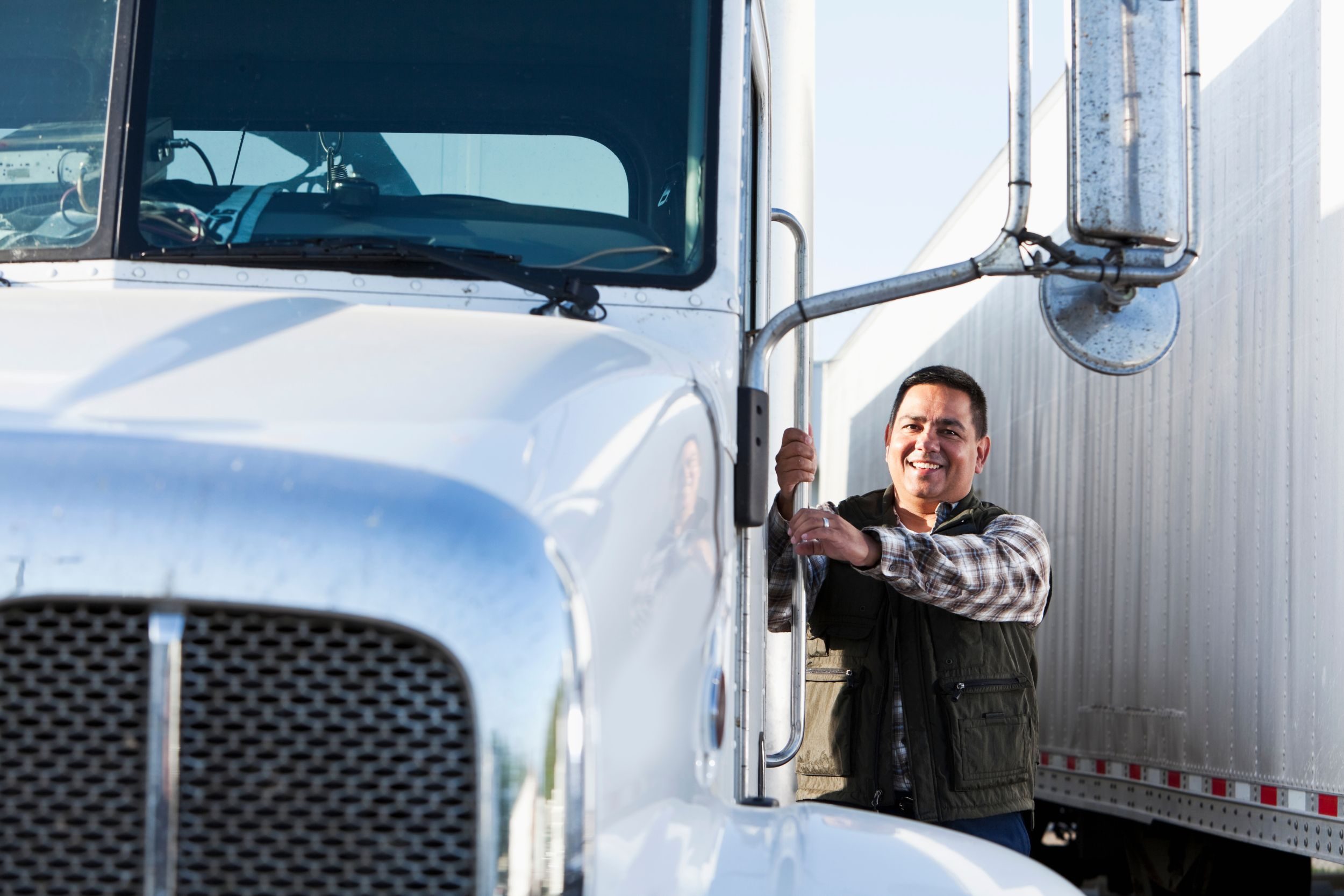 A truck driver holding on to the side of his truck and smiling at the camera