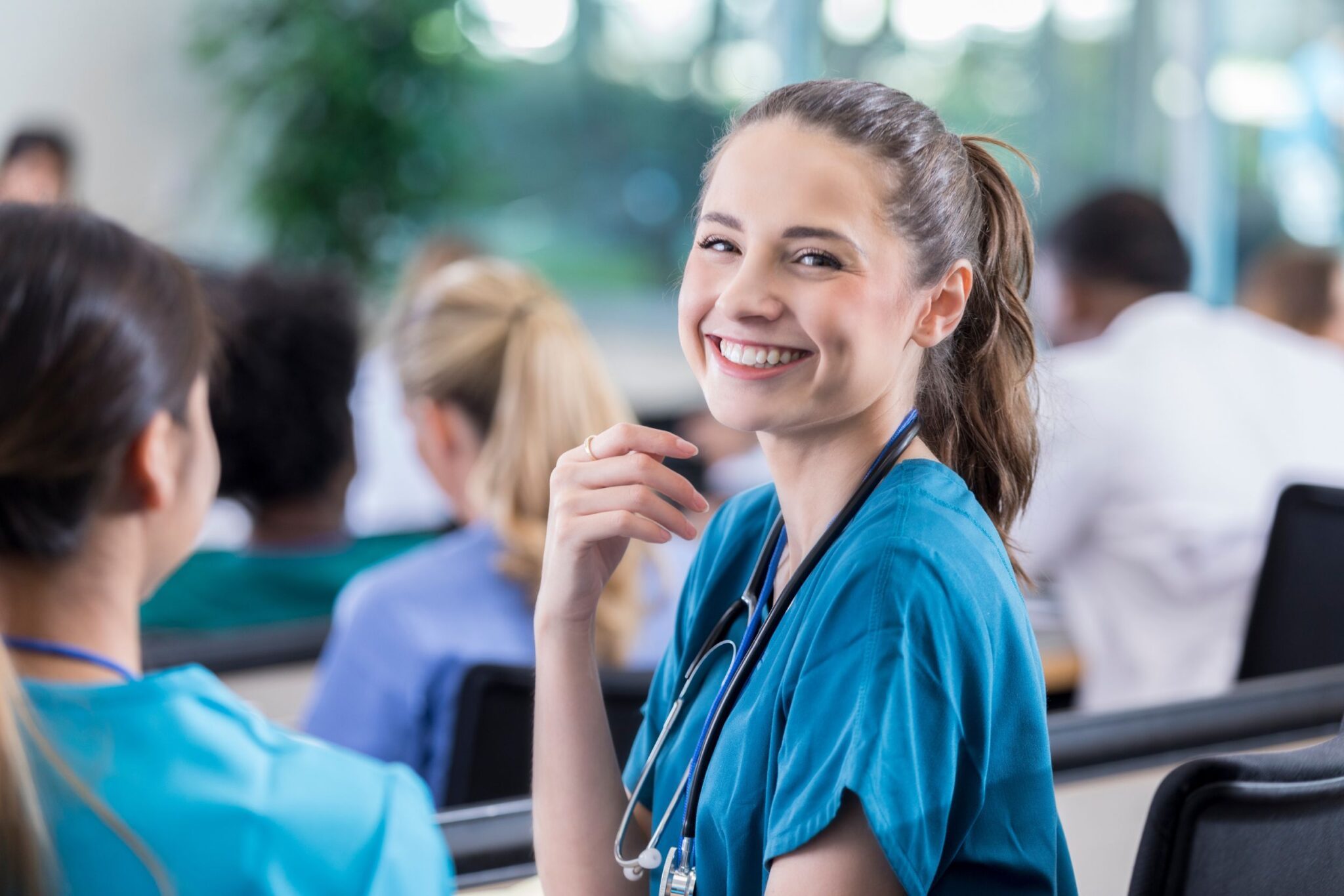 A young nurse smiling at the camera in a room full of nurses