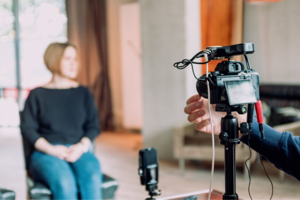 A cameraman recording a woman sitting in a chair